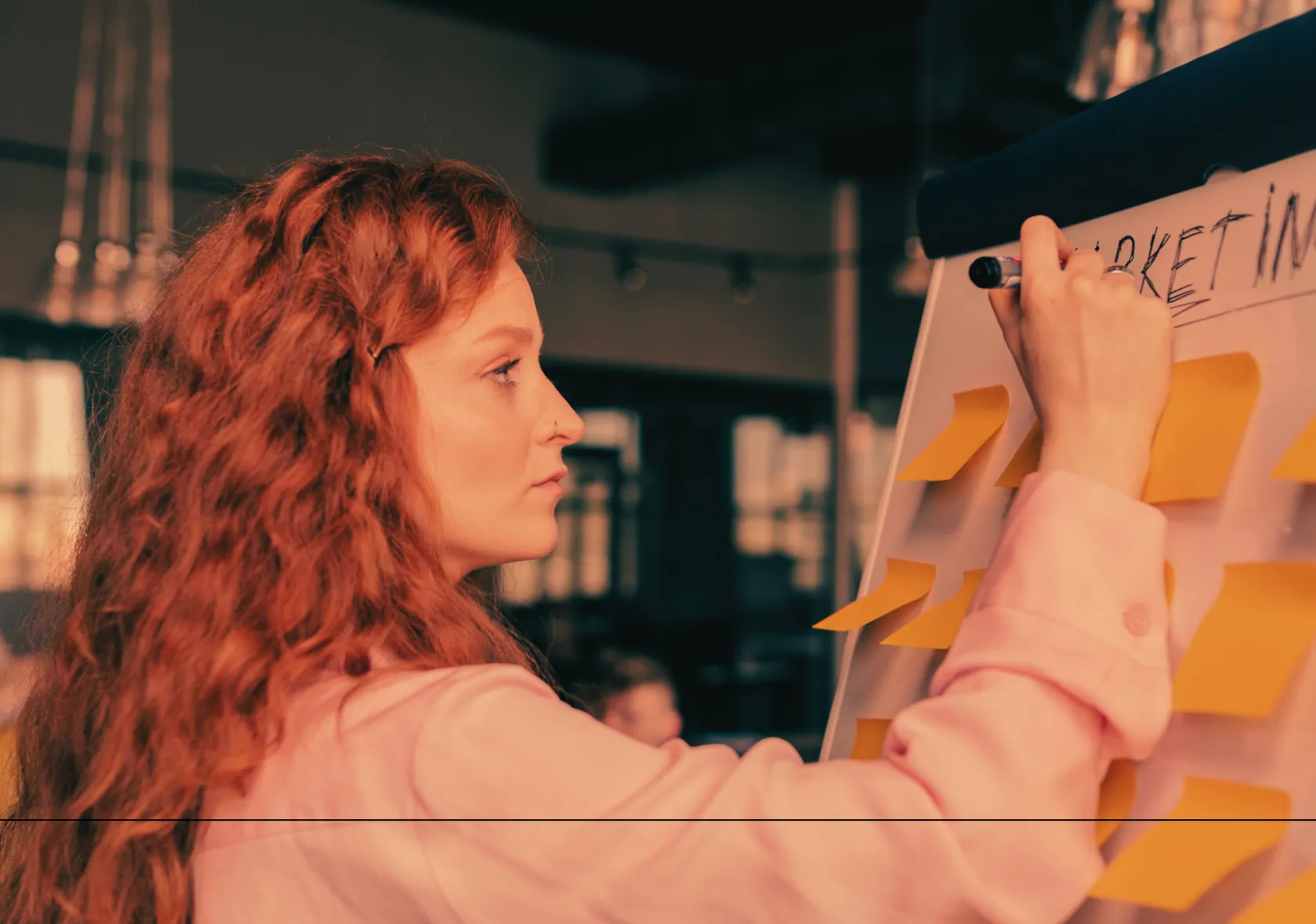 “A focused woman with long red hair writing on a flipchart covered in yellow sticky notes, symbolizing strategic planning and creative problem-solving.”